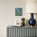 Gray console table with decorative items including a blue lamp, books, and a small sculpture, with a colorful abstract painting on the wall.