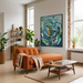 True Blue, a Blue and Green Abstract Mid CEntury Modern Geometric Print by Leah NAdeau featuring a swirling pattern of teal, blue, green, and white shapes, hanging on a light gray wall in a modern living room setting with an orange sofa and wooden coffee table.