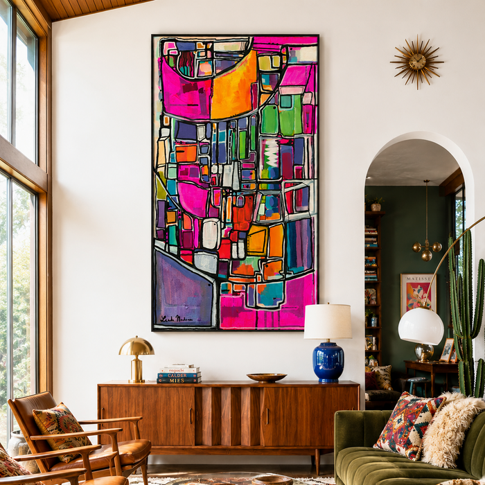 A large framed abstract canvas print with a vibrant mid-century modern geometric pattern in pink, orange, green, yellow, and blue, displayed on a white wall in a cozy living room setting. Nevertheless She Persisted by artist Leah Nadeau in Portland Oregon