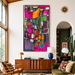 A large framed abstract canvas print with a vibrant mid-century modern geometric pattern in pink, orange, green, yellow, and blue, displayed on a white wall in a cozy living room setting. Nevertheless She Persisted by artist Leah Nadeau in Portland Oregon