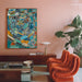 A modern living room scene featuring a large, colorful abstract geometric painting on a dusty pink wall. Below the painting is a dark wood console table with a white table lamp, and in the foreground is a low glass coffee table.