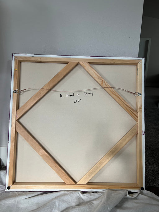 The painting "A Friend of Dorothy" by leahnadeau is displayed, showcasing its wooden framing and attached hanging wire. Inscribed with the title "A Friend of Dorothy" and the year "2021," this artwork is part of the LGBTQ art collection. It is positioned against a white wall, with a portion of a carpeted floor visible.